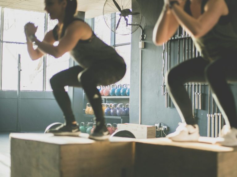 Zwei Frauen führen Squats auf Holzkisten in einer Sportphysiotherapie aus.
