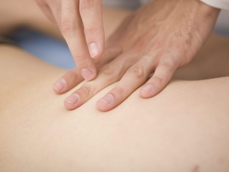 Eine Hand führt eine Therapieanwendung auf dem Körper einer Person durch.